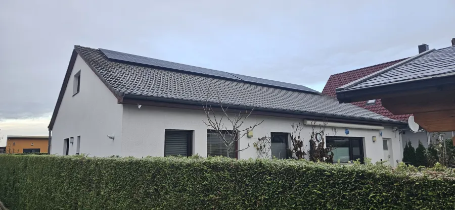 Siedlungshaus mit Photovoltaik hinter einer Hecke